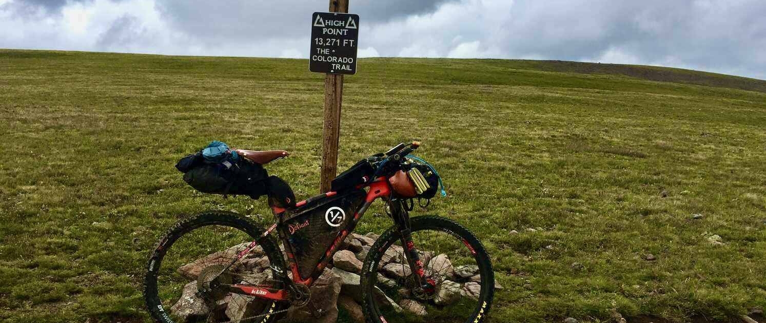 Bikepacking bike next to the Coney Summit sign, the highest point on the Colorado Trail Race (CTR), where altitude sickness can be a challenge.