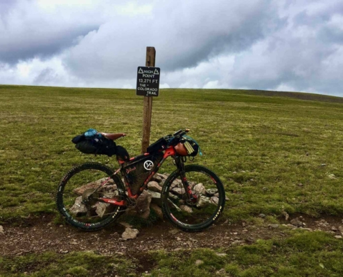 Bikepacking bike next to the Coney Summit sign, the highest point on the Colorado Trail Race (CTR), where altitude sickness can be a challenge.
